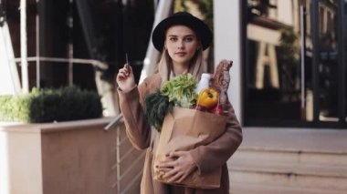 Paket ürünler ve tutar kredi kartı ile sokakta şık ceket ayakta giyen genç güzel kadın. Alışveriş, sağlıklı beslenme, internet salonu konsept.