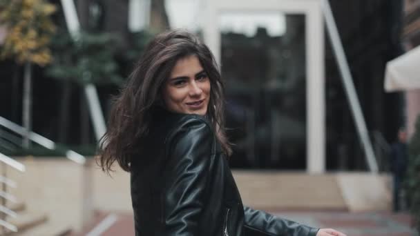 Mladá atraktivní žena obrací na kameru dvakrát s milým úsměvem chůzi na ulici nedaleko moderní budova — Stock video