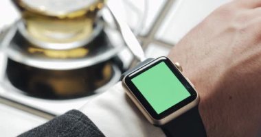 Adam el jestleri modern smartwatch kullanımda kafede yeşil bir ekran ile kapatın. Bir fincan çay içinde belgili tanımlık geçmiş. İş adam Internet mesaj teknoloji