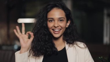 Güzel genç kadın rahat kafede Ok ve gülümseyerek ayakta gösterir. İş yerinde genç kız Tamam işareti