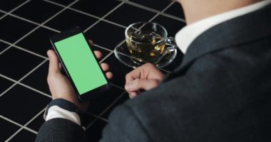 Genç işadamı kullanım smarthpone yeşil ekran dokunmatik yüzey ve el hareketi ile kafede kapatın. Hücresel, adam dokunarak ve gözatma sayfası tarafından kaydırma ve okuma Haberler