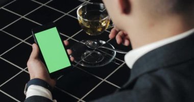 Genç işadamı kullanım smarthpone yeşil ekran dokunmatik yüzey ve el hareketi ile kafede kapatın. Hücresel, adam dokunarak ve gözatma sayfası tarafından kaydırma ve okuma Haberler