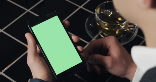 Jonge zakenman gebruik smarthpone met greenscreen touchpad en gebaren close-up in café. Guy holding cellulaire, aftappen en scrollen door de bladeren van de pagina's en lees nieuws — Stockvideo