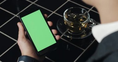 Genç işadamı kullanım smarthpone yeşil ekran dokunmatik yüzey ve el hareketi ile kafede kapatın. Hücresel, adam dokunarak ve gözatma sayfası tarafından kaydırma ve okuma Haberler