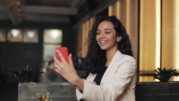Σύγχρονη επιχείρηση γυναίκα μιλάτε στο τηλέφωνο έχοντας συνομιλία μέσω βίντεο chat διάσκεψη στο φιλόξενο café. Χρησιμοποιώντας το smartphone app στο smartphone χαμογελά ευτυχισμένη γυναίκα των επιχειρήσεων — Αρχείο Βίντεο