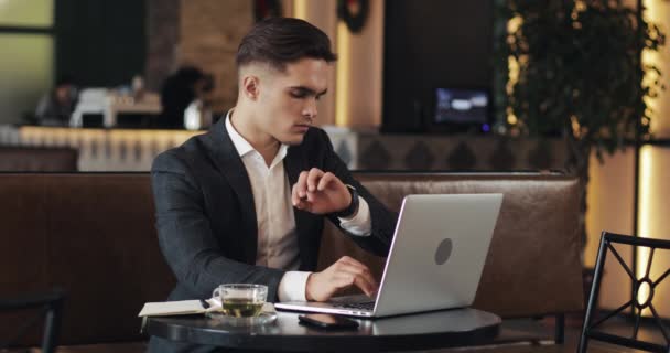 Mladý podnikatel v moderní kanceláři nebo společně pracovat a pomocí chytré hodinky. Freelancer mluví s smartwatch a psaní v programu Poznámkový blok. 4k Uhd.