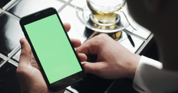 Young businessman use smarthpone with greenscreen touchpad and gesturing close up in cafe. Guy holding cellular, tapping and scrolling by the browsing pages and read news — Stock Video