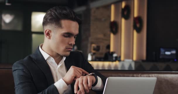 Νεαρός επιτυχημένος επιχειρηματίας με smartwatch που κάθεται στο καφενείο. Freelancer Δείτε τα μηνύματα, ενεργοποίηση των εφαρμογών, ρυθμίστε τις εφαρμογές — Αρχείο Βίντεο