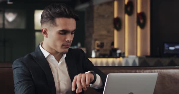 Jovem empresário de sucesso com smartwatch sentado no café. Freelancer ver as mensagens, ativar os aplicativos, ajustar os aplicativos, falando com um smartwatch — Vídeo de Stock