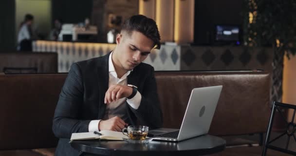 Jeune homme d'affaires prospère avec smartwatch assis dans un café. Freelance afficher les messages, activer les applications, ajuster les applications, parler à une smartwatch — Video