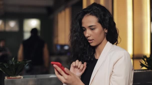 Bela jovem empresária usando smartphone no café acolhedor. Menina sorrindo e conversando online com seus amigos — Vídeo de Stock