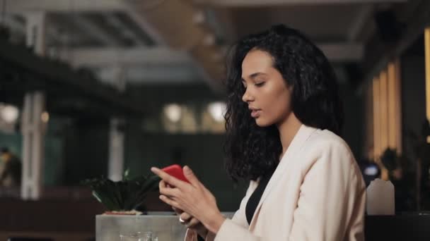 Bela jovem empresária usando smartphone no café acolhedor. Menina sorrindo e conversando online com seus amigos — Vídeo de Stock