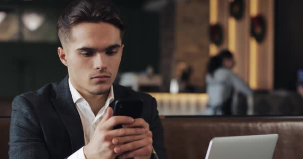 Bell'uomo che usa lo smartphone seduto in un bar o in un ufficio di coworking. Ritratto di imprenditore di successo — Video Stock