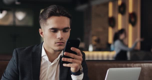 Jovem empresário trabalhando no smartphone sentado no café aconchegante — Vídeo de Stock