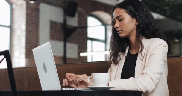 Jovem mulher de negócios trabalha em um laptop no escritório moderno. Ela ri encantadoramente — Vídeo de Stock