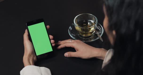 Νεαρή γυναίκα χρήση smartphone με πράσινη οθόνη και να πιείτε καφέ. Οθόνη αφής στην οθόνη μαύρο πράσινο smartphone. Χρησιμοποιώντας το smartphone, το κορίτσι κρατά smartphone με πράσινη οθόνη — Αρχείο Βίντεο