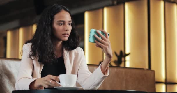 Kahve içme ve tarassut video üstünde onun smartphone rahat kafede oturan iş kadın — Stok video