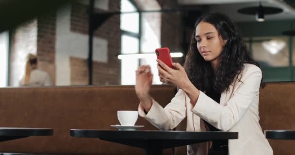 Vacker ung affärskvinna i rosa färg med smartphone och dricker kaffe på mysiga café eller moderna kontor — Stockvideo