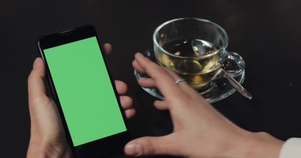 Νέοι επαγγελματίες γυναίκα χρήση smartphone με πράσινη οθόνη touchpad και χειρονομώ κοντινό καφέ. Κορίτσι εκμετάλλευση κινητής τηλεφωνίας, περνώντας από τις σελίδες περιήγησης και διαβάστε ειδήσεις — Αρχείο Βίντεο