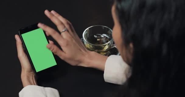 Junge Geschäftsfrau benutzt Smarthpone mit Greenscreen-Touchpad und gestikuliert aus nächster Nähe im Café. Mädchen hält Handy, tippt und blättert durch die Browserseiten und liest Nachrichten — Stockvideo