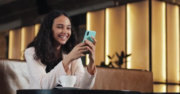 Affärskvinna med smartphone i café dricka kaffe skrattar i café. Kommunikation, framgångsrikt företag, dejting, gott humör koncept — Stockvideo