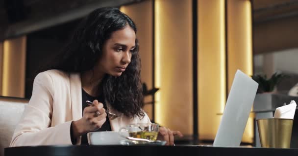 Femme d'affaires assis avec un ordinateur portable dans le café et dîner avec une tasse de thé sur la table. Déjeuner au bureau — Video