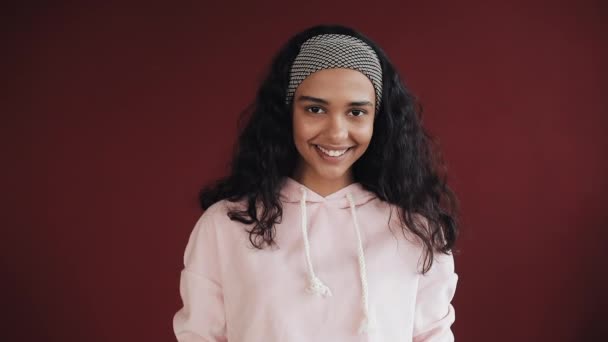 Retrato de una hermosa chica vestida con pijama rosa mirando a la cámara sobre el fondo rojo. Ella sonríe. — Vídeos de Stock