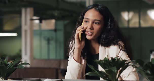 Jovem empresária falando ao telefone enquanto está sentada no café. Ela está sorrindo. Menina bonita ter conversa casual no telefone móvel — Vídeo de Stock