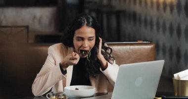 Bir dizüstü bilgisayar kafede oturan ve bir fincan çay ile akşam yemeği masada yemek bir iş kadını. Çalışma masası yemek