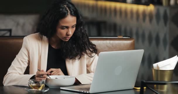 Mulher de negócios sentada com um laptop no café e jantando com uma xícara de chá na mesa. Almoçar na mesa de trabalho — Vídeo de Stock