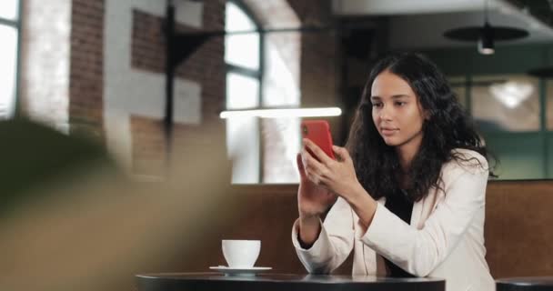 Mujer de negocios utilizando la aplicación en el teléfono inteligente sentado en la oficina moderna. Hermosa profesional femenina casual en traje rosa que tiene buenas noticias en el teléfono inteligente — Vídeo de stock