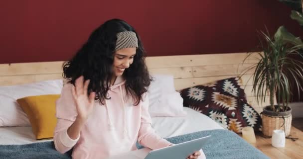 Jovem mulher bonita sentada na cama em casa aconchegante feliz conversando com alguém em uma chamada de vídeo em seu laptop — Vídeo de Stock