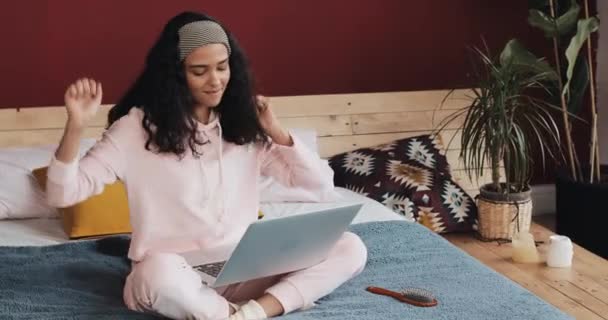 Aantrekkelijk meisje plezier zittend op het bed met laptop. Ze zingt, danst, verheugt zich op goed nieuws — Stockvideo