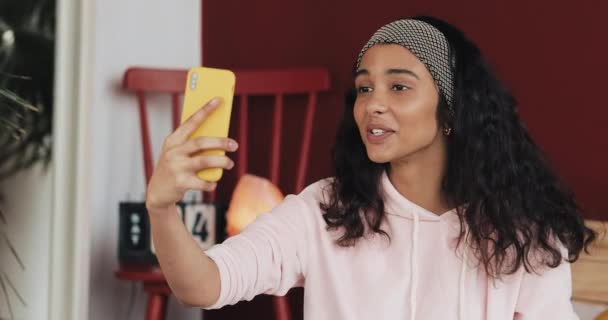 Glad African American tjej gör videosamtal med gula smartphone ringer vänner pratar sittande på sängen — Stockvideo