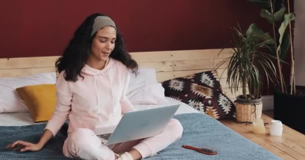 Aantrekkelijk meisje plezier zittend op het bed met laptop. Ze zingt, danst, verheugt zich op goed nieuws — Stockvideo