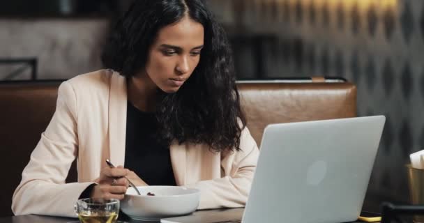 Obchodní žena sedí s přenosným počítačem v kavárně a jíst večeři s šálkem čaje na stole. Obědváme na pracovní stůl — Stock video