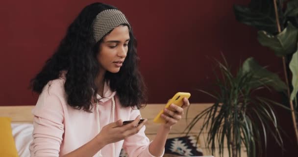 Menina atraente segurando cartão de crédito e usando smartphone na cama. Jovem feliz compras on-line com telefone celular e cartão de crédito. Conceito de compras online — Vídeo de Stock