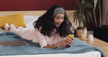 Mutlu Afro-Amerikan kız sohbet ve metin mesajlaşma Smartphone cep telefonu ile evde yatakta yatıyordu. Genç kadın Smartphone cep telefonu ile iyi haber alır