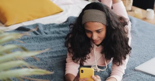 幸せなアフリカ系アメリカ人女の子は喜んで彼女の黄色のスマート フォンでビデオ通話で彼女の友達とおしゃべりベッドの上の彼女の腹にあります。 — ストック動画