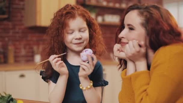 Een moeder en haar dochter schilderen paaseieren in een gezellige keuken. Ze lachen en hebben plezier. Gelukkige familie bereidt zich voor op Pasen. Gelukkig Pasen — Stockvideo