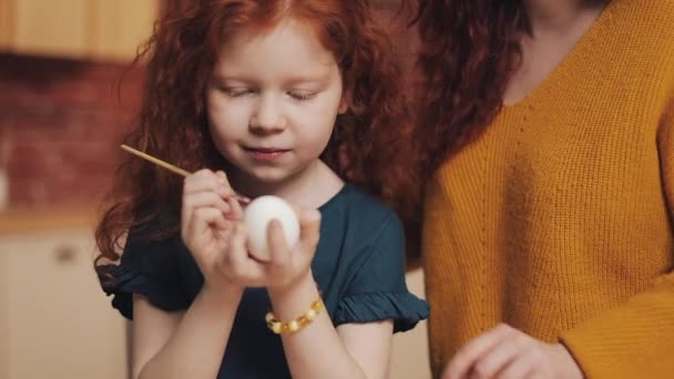 Una madre y su hija pintando huevos de Pascua en la acogedora cocina. Se ríen y se divierten. Familia feliz preparándose para la Pascua. Feliz Pascua. — Vídeos de Stock