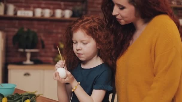 母親と娘は居心地の良いキッチンでイースターエッグを描いています。彼らは笑って楽しんでいます。イースターの準備をしている幸せな家族。ハッピー・イースター — ストック動画