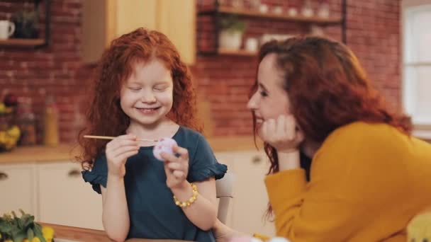 Una madre y su hija pintando huevos de Pascua en la acogedora cocina. Se ríen y se divierten. Familia feliz preparándose para la Pascua. Feliz Pascua. — Vídeos de Stock