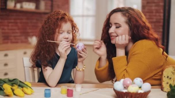 Eine Mutter und ihre Tochter bemalen Ostereier in der gemütlichen Küche. Sie lachen und haben Spaß. Glückliche Familie bereitet sich auf Ostern vor. Frohe Ostern — Stockvideo