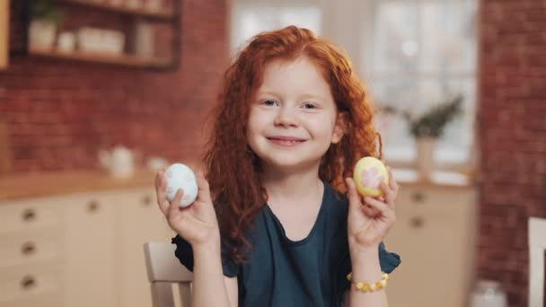 一个快乐的红头发小女孩在厨房背景上玩复活节彩蛋的画像。她在欢呼，在镜头前玩得很开心。复活节快乐 — 图库视频影像