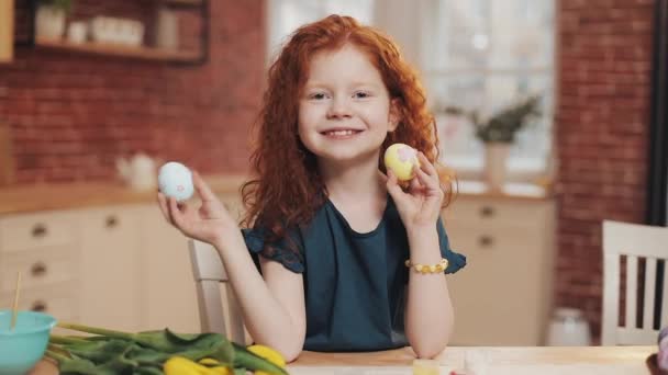 Ritratto di allegra rossa bambina che gioca con l'uovo di Pasqua sullo sfondo della cucina. Sta facendo il tifo e si sta divertendo alla telecamera. Buona Pasqua — Video Stock