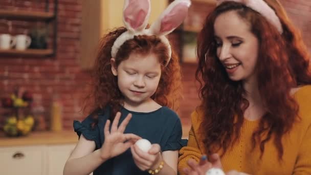 Een moeder en haar dochter schilderen paaseieren in een gezellige keuken. Ze lachen en hebben plezier. Gelukkige familie bereidt zich voor op Pasen. Gelukkig Pasen — Stockvideo