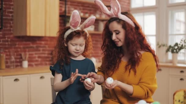 Matka i jej córka malują wielkanocne jajka w przytulnej kuchni. Śmieją się i dobrze się bawią. Szczęśliwa rodzina przygotowuje się do Wielkanocy. Wesołych Świąt — Wideo stockowe