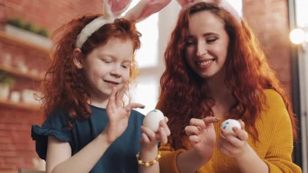 Matka a její dcera malují velikonoční vajíčka v útulné kuchyni. Smějí se a baví se. Šťastná rodina se připravuje na Velikonoce. Veselé Velikonoce — Stock video