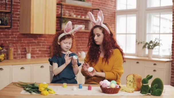 A mother and her daughter painting Easter eggs in cozy kitchen. They laughing and have fun. Happy family preparing for Easter. Happy easter — Stock Video